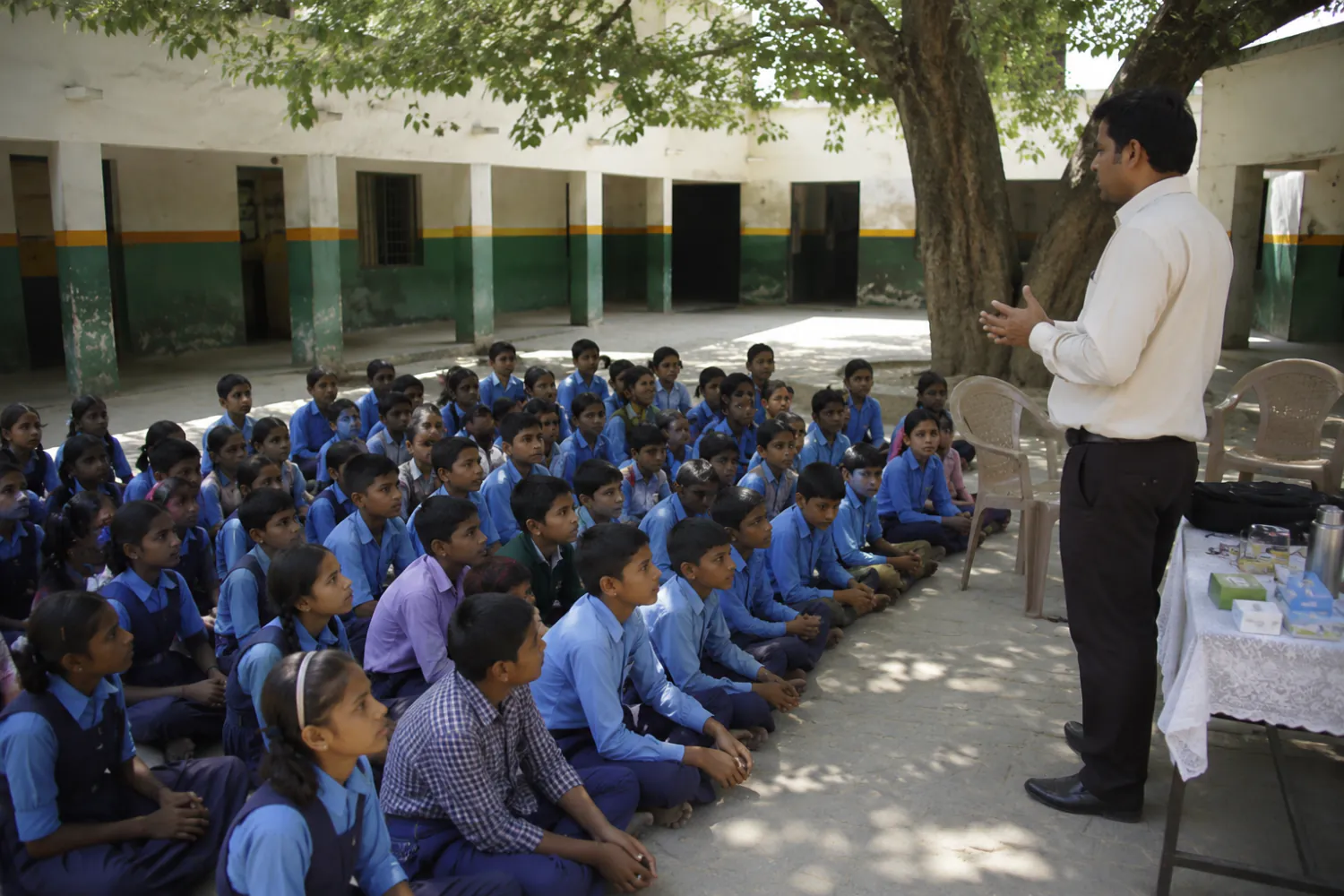 Illustration: schoolchildren seated in a courtyard listening to a health-education session